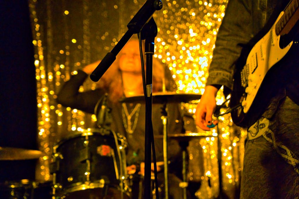 Schlagzeuger auf der Bühne, umgeben von glänzendem Hintergrundlicht.