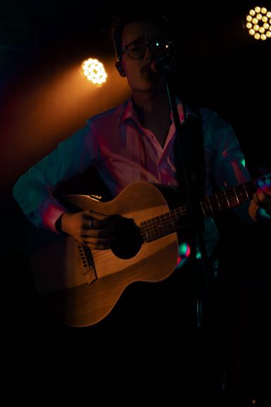 Mann spielt Gitarre auf einer Bühne mit bunten Lichtern im Hintergrund.