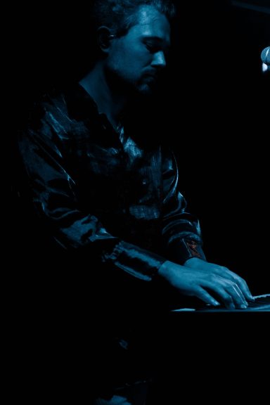 Mann spielt Klavier in dunkler, blauer Beleuchtung.