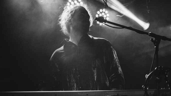 Ein Musiker steht an einem Keyboard, umgeben von Nebel und Lichtstrahlen.