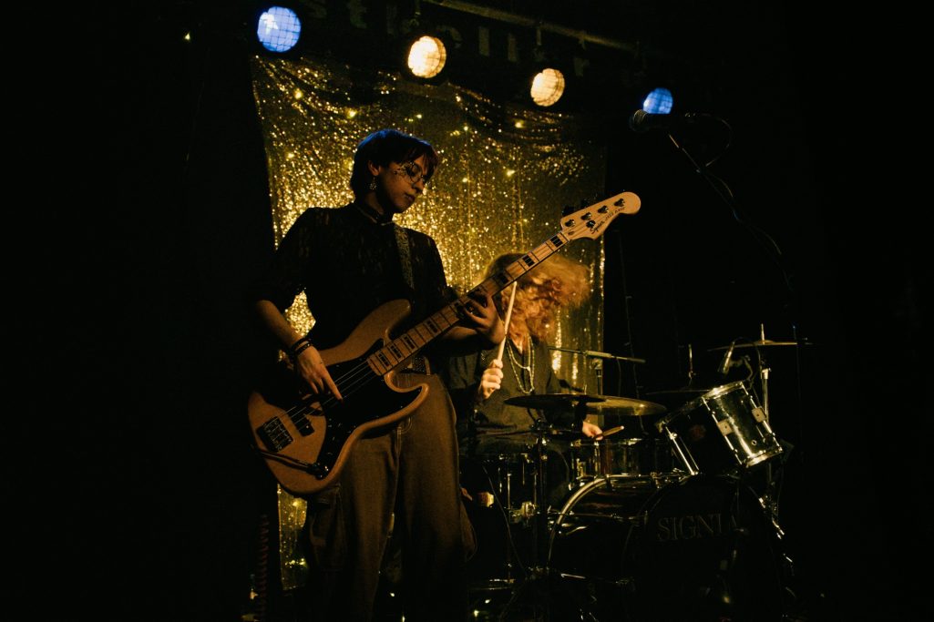 Zwei Musiker spielen live auf der Bühne, einer am Schlagzeug, der andere an der E-Gitarre.