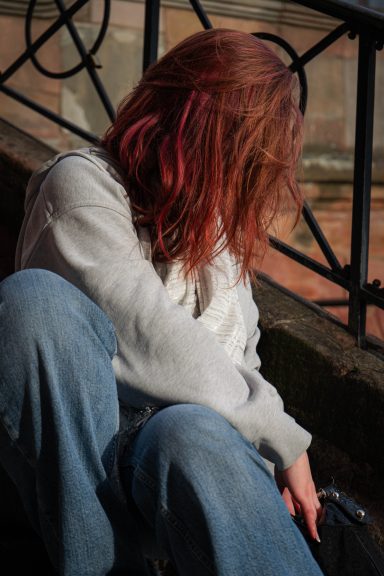 Eine Person mit langen, roten Haaren sitzt nachdenklich an einem Geländer.