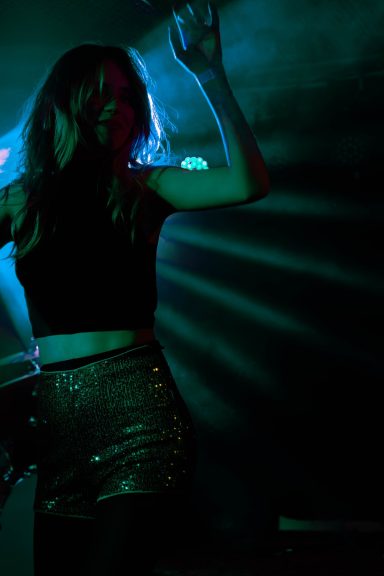 Tanzende Frau in schwarzem Oberteil und glitzerndem Rock unter bunten Lichtern.