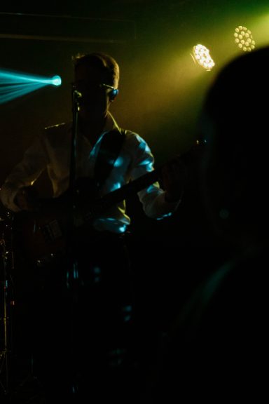Ein dunkel beleuchteter Musiker spielt Gitarre auf der Bühne.