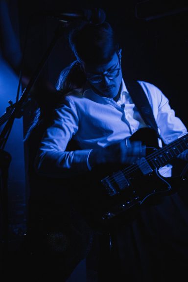 Musiker spielt Gitarre auf der Bühne in gedämpftem blauen Licht.