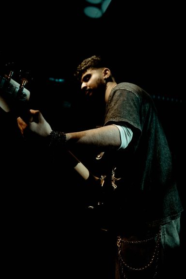 Mann spielt Gitarre auf einer dunklen Bühne, konzentriert und kreativ.