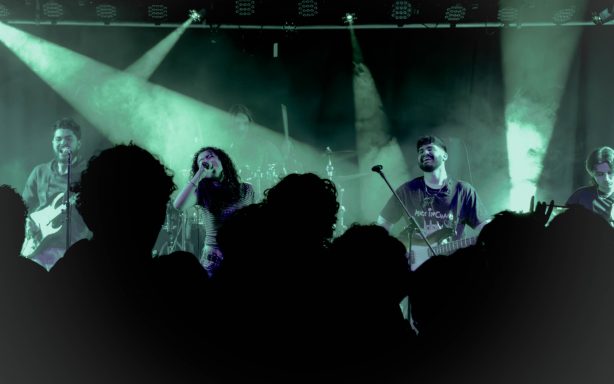 Band spielt live auf der Bühne vor einem begeisterten Publikum im Halbdunkel.