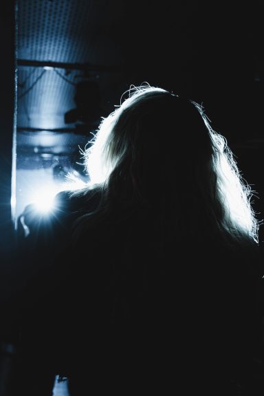Silhouette einer Person mit langem, hellem Haar vor hellen Lichtern.