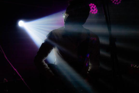 Silhouette eines Musikers vor bunten Lichtern auf der Bühne.