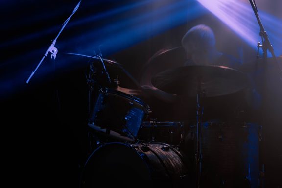Dunkle Silhouette eines Schlagzeugers mit Lichstrahlen im Hintergrund.
